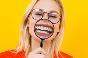 woman in glasses holding magnifying glass over teeth