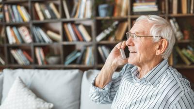 retiree sits on sofa in front of book cases while talking on phone