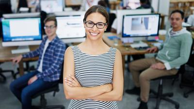 female intern poses in front of computers stations and other interns