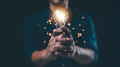 man holds a lightbulb with sparkles in a dark room