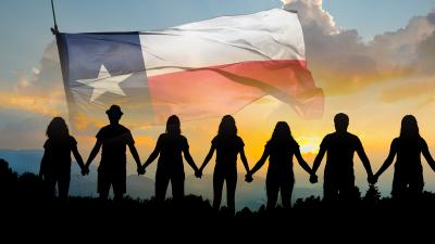 seven adults hold hands in front of a Texas flag and sunrise