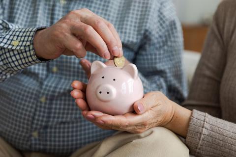 hand adds coins to a small piggy bank