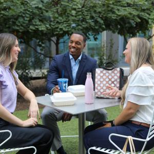 Three people sitting at a white outdoor table in a courtyard