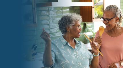 two women in a kitchen dance and sing with wooden spoons