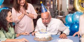 man blows out candles on his birthday cake with friends