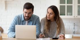 young couple at home looks at laptop screen together
