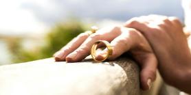 Hands resting on hand rail with wedding band looped around fingertip