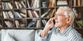 retiree sits on sofa in front of book cases while talking on phone