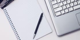 spiral notebook and pen next to laptop keyboard