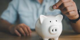 man drops coins into a white piggy bank