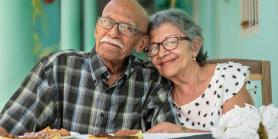 older couple sits at table with plates smiling at camera