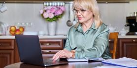 older woman sit at kitchen table while viewing a webinar