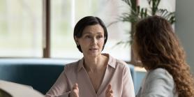 two women talk at a desk