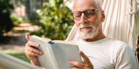 man in glasses reads a book in a hammock