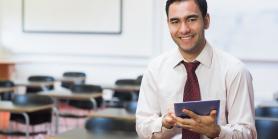 male teacher with tablet in empty classroom