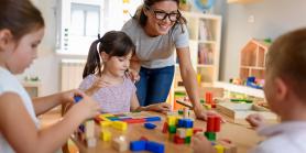 preschool teacher helps children build with blocks