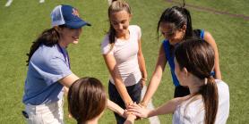 coach and four students stack their hands on the field