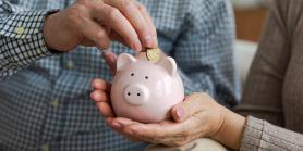 hand adds coins to a small piggy bank