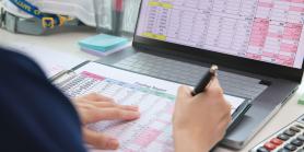person sits at desk with a ledger spreadsheet and laptop