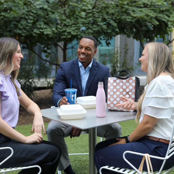 Three people sitting at a white outdoor table in a courtyard