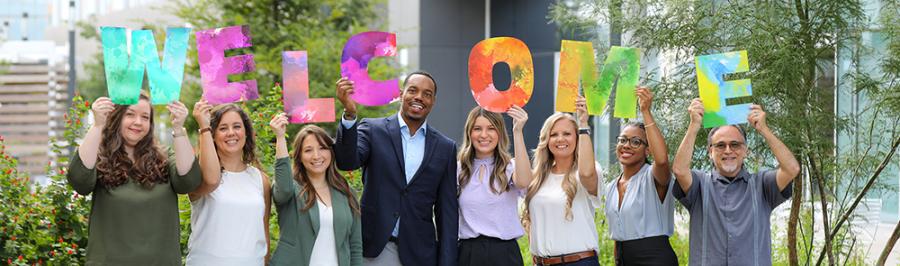 eight professionals hold up the letters to spell welcome