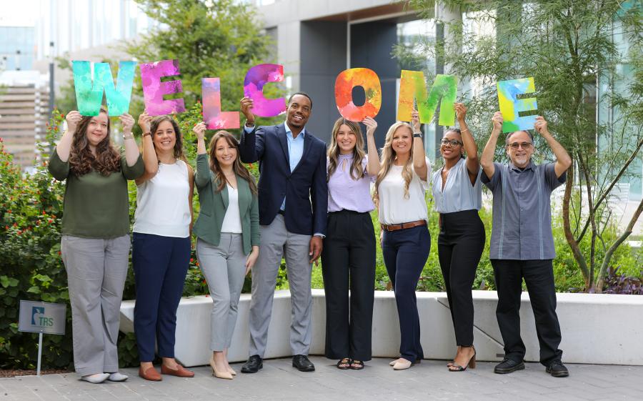coworkers outside holding up signs that spell out welcome