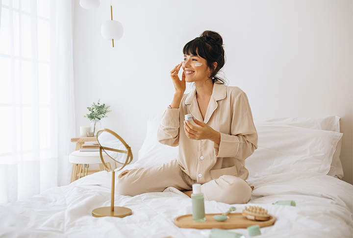 woman sits on bed while completing skincare routine