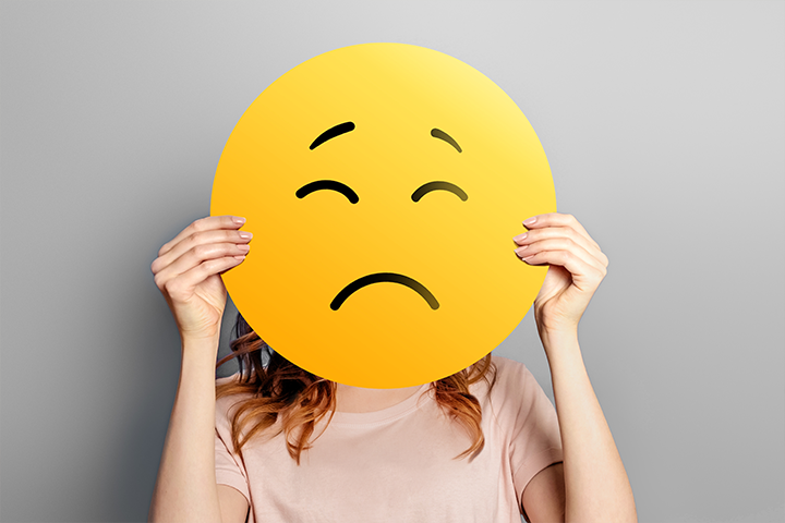 person holding sad face emoji over face