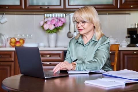 older woman sit at kitchen table while viewing a webinar