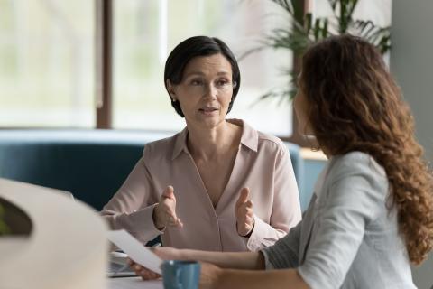 two women talk at a desk