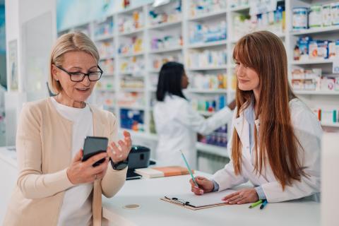 woman talks to pharmacist while looking at phone
