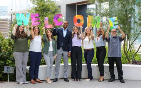 coworkers outside holding up signs that spell out welcome
